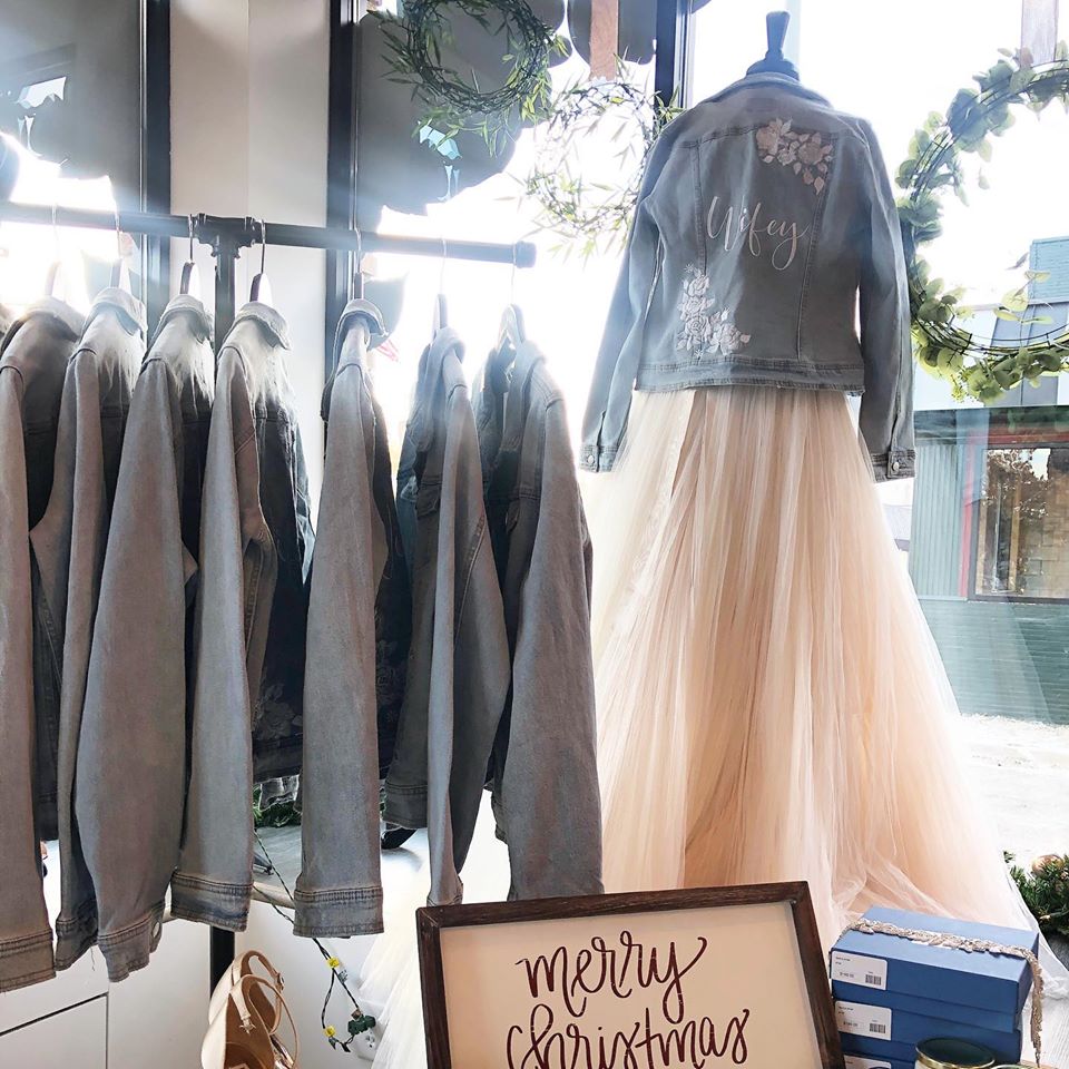 A rack of embroidered jean jackets and one jean jacket on the mannequin over a wedding dress
